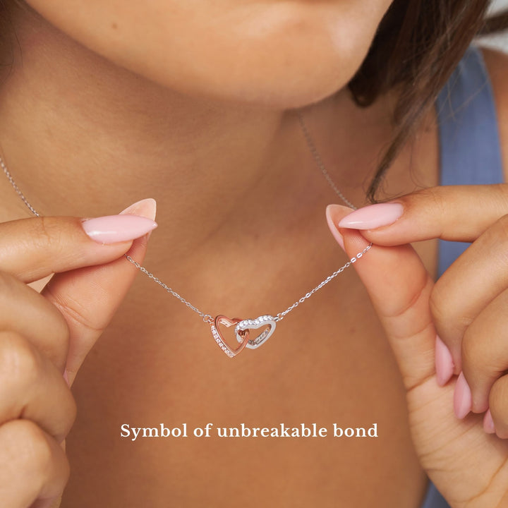 Necklace with interlocking heart pendants held by hands, labeled 'Symbol of unbreakable bond'.