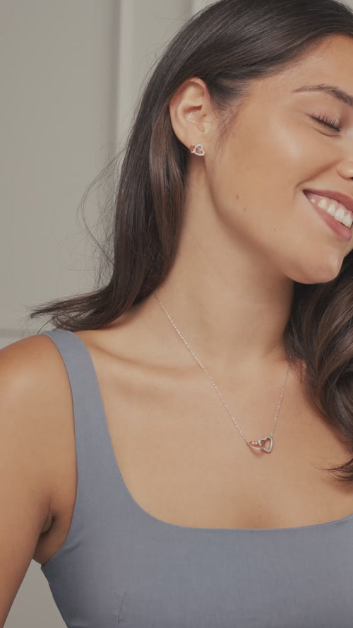 A woman wearing and showing an interlocking hearts necklace and earrings.